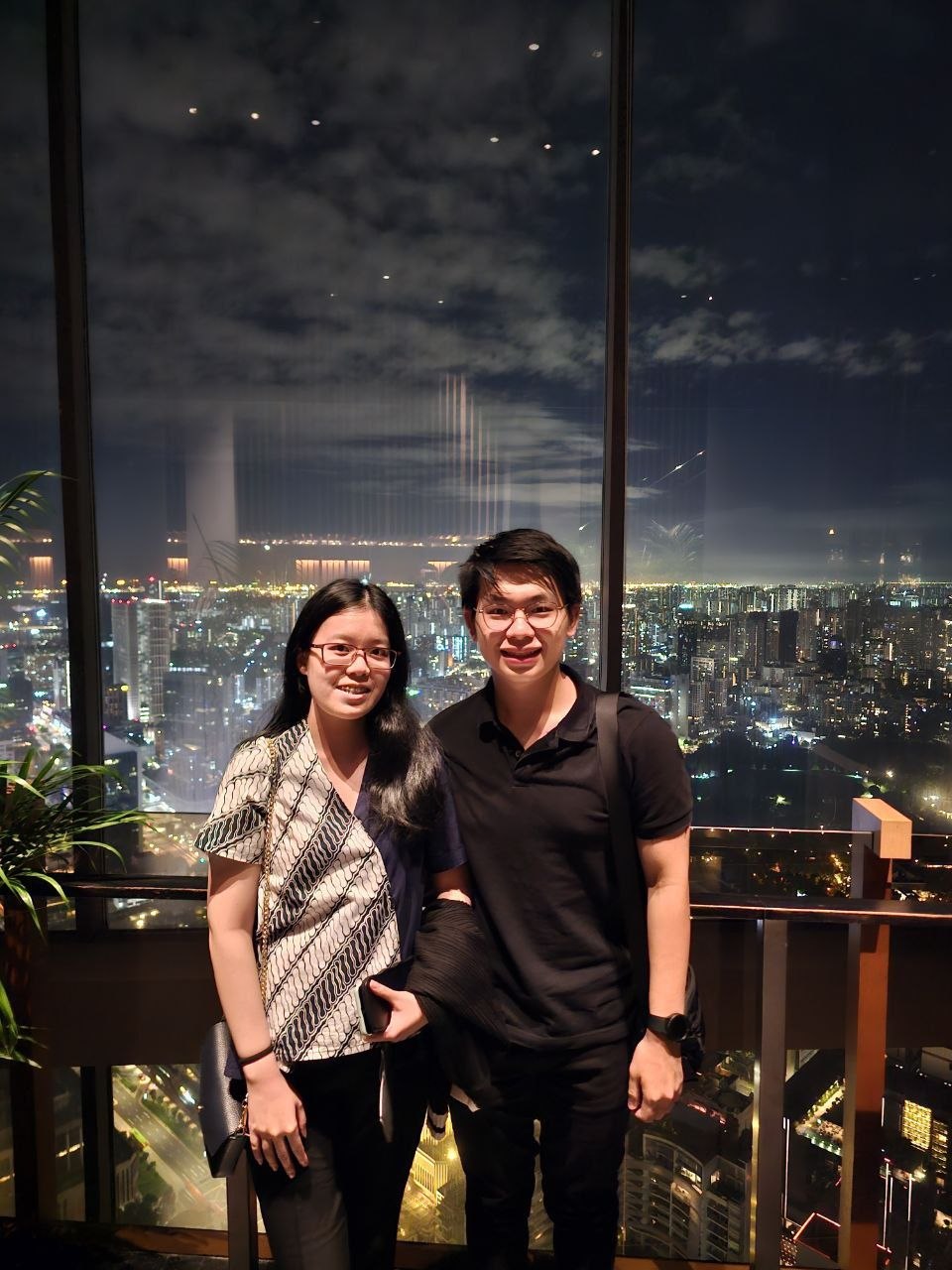 Rey and Feli standing together at night with a city skyline glowing behind them