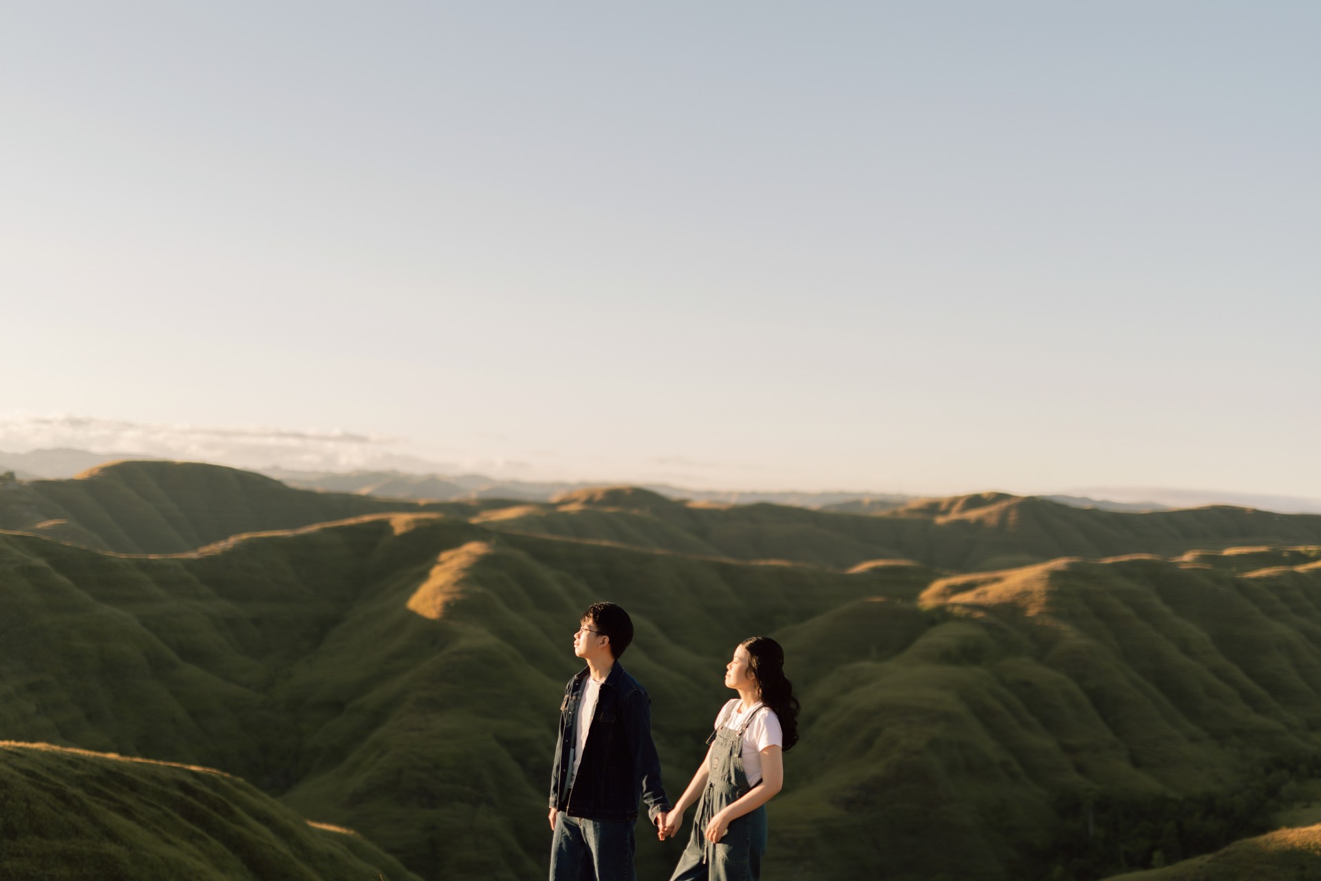 Rey and Feli holding hands before a sweeping view of rolling green hills