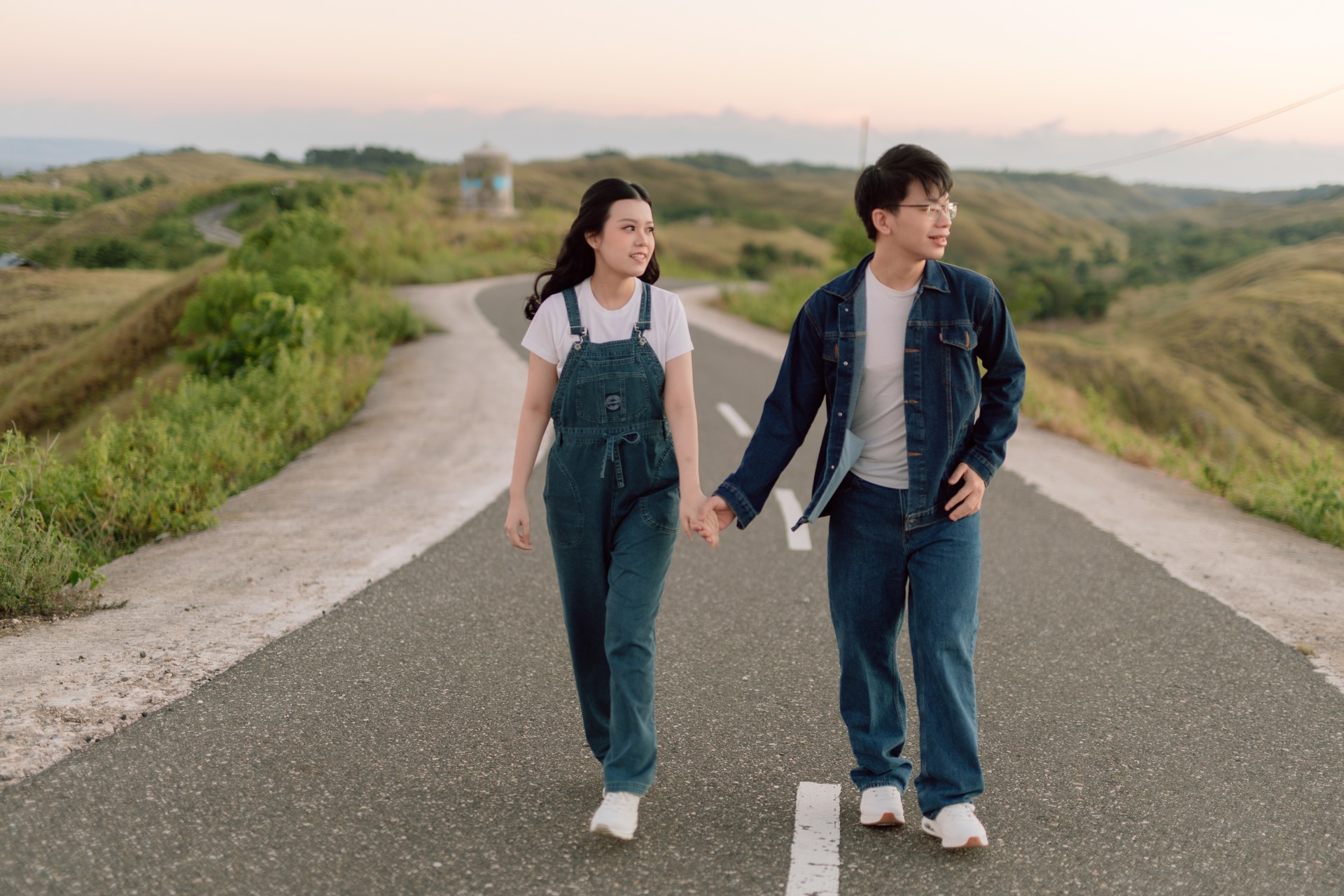 Rey and Feli wearing denim and holding hands as they walk along a winding road