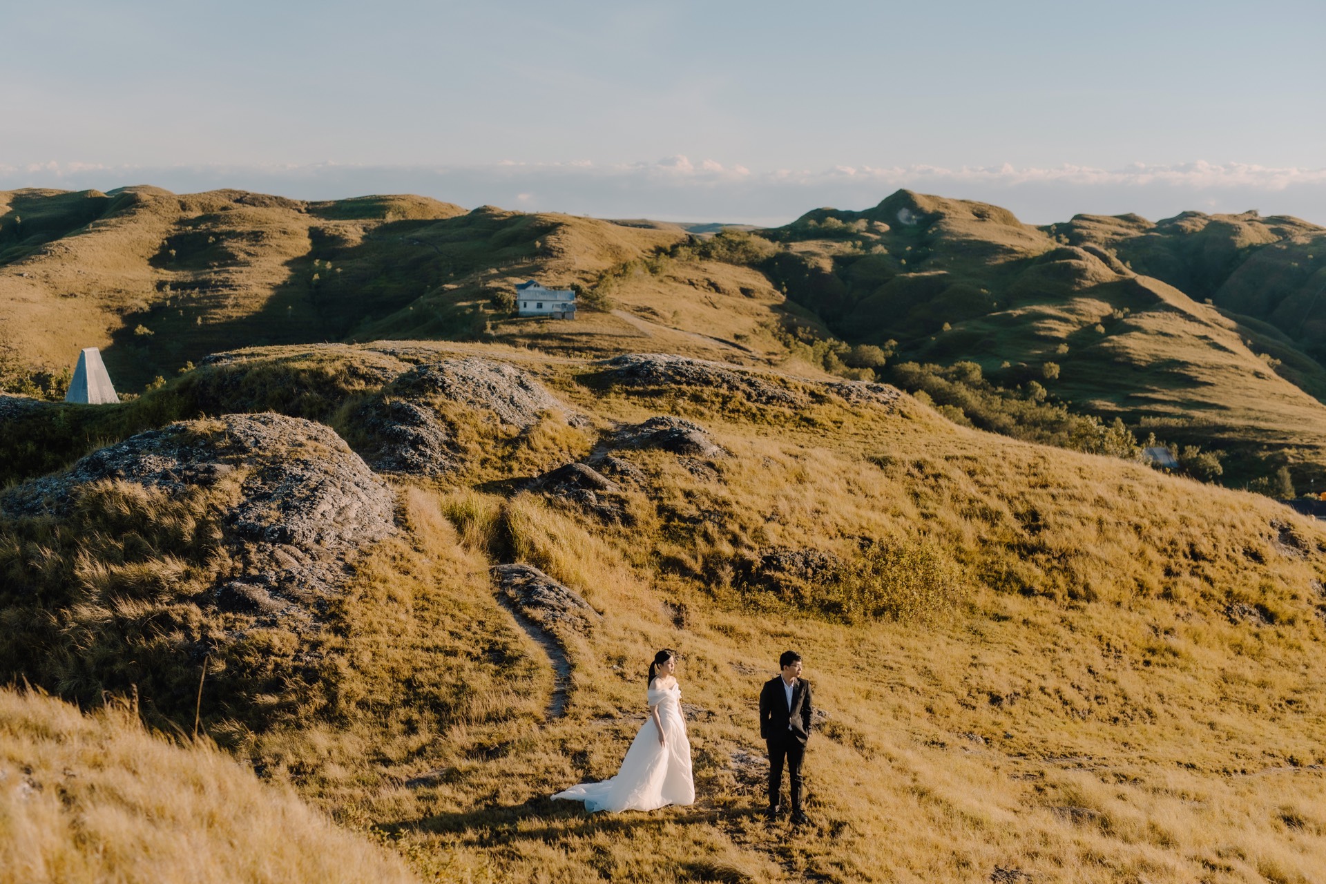 Rey and Feli standing together in wedding attire among wide golden hills