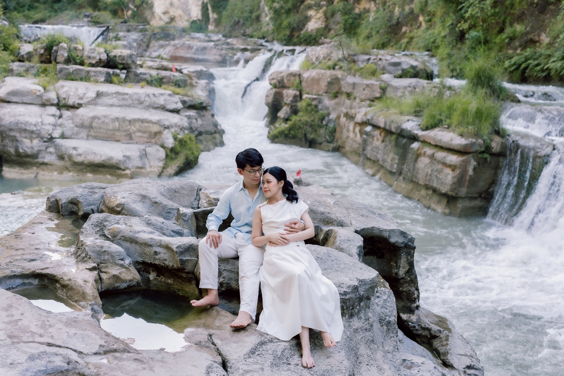 Rey and Feli sitting close together among the rocks beside a waterfall