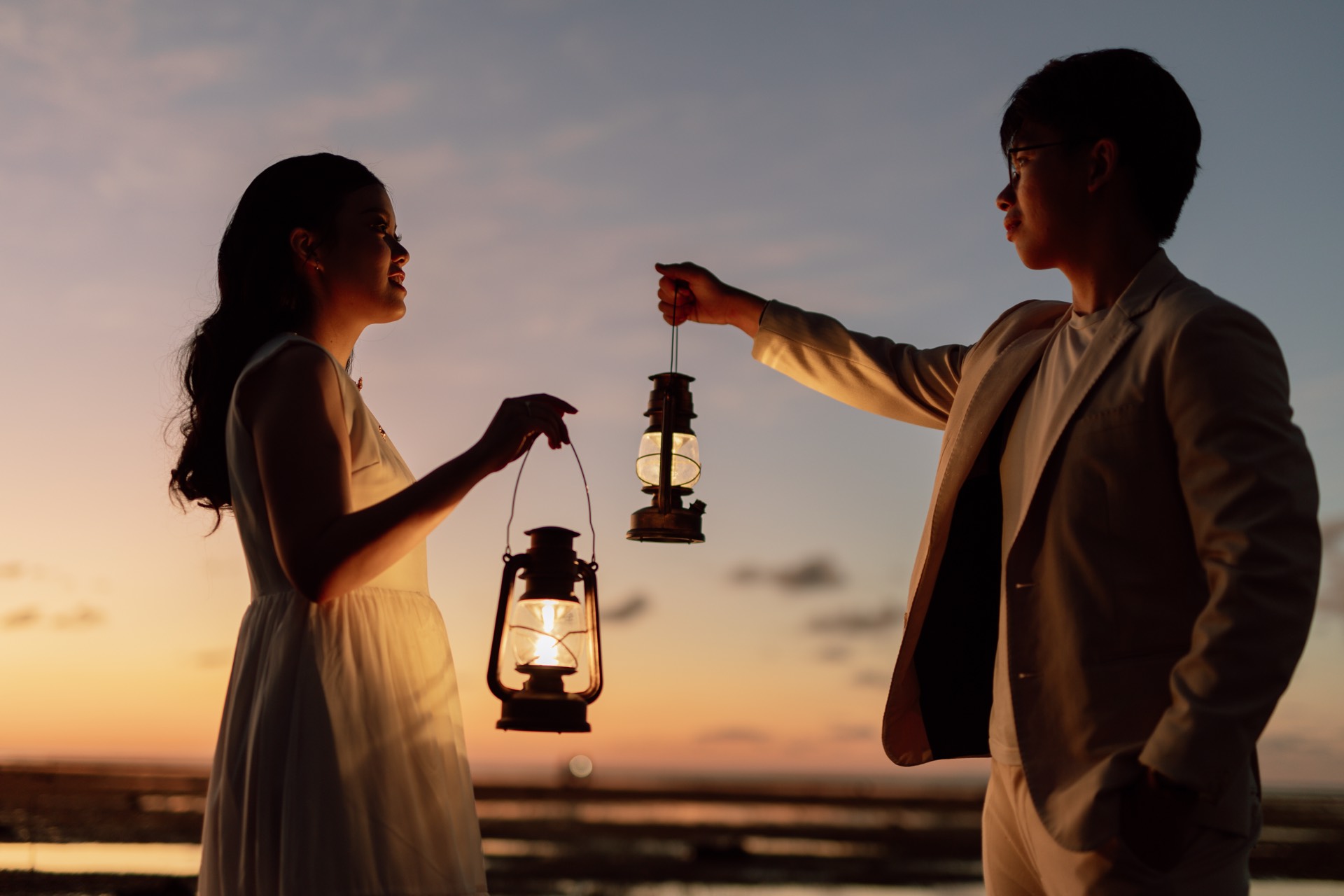 Rey and Feli holding glowing lanterns opposite each other at sunset