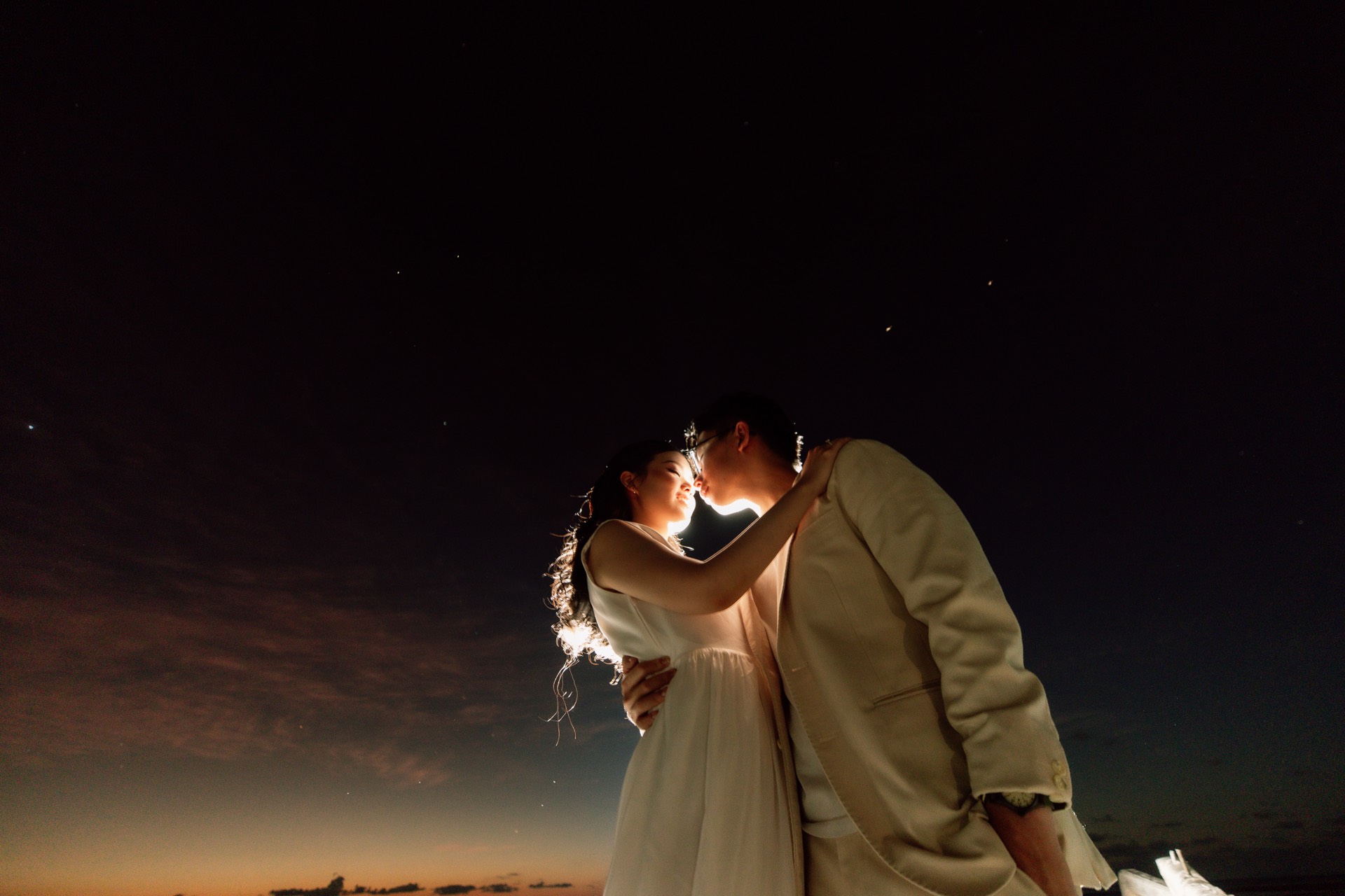 Rey and Feli kissing beneath a dark sky with a warm light behind them