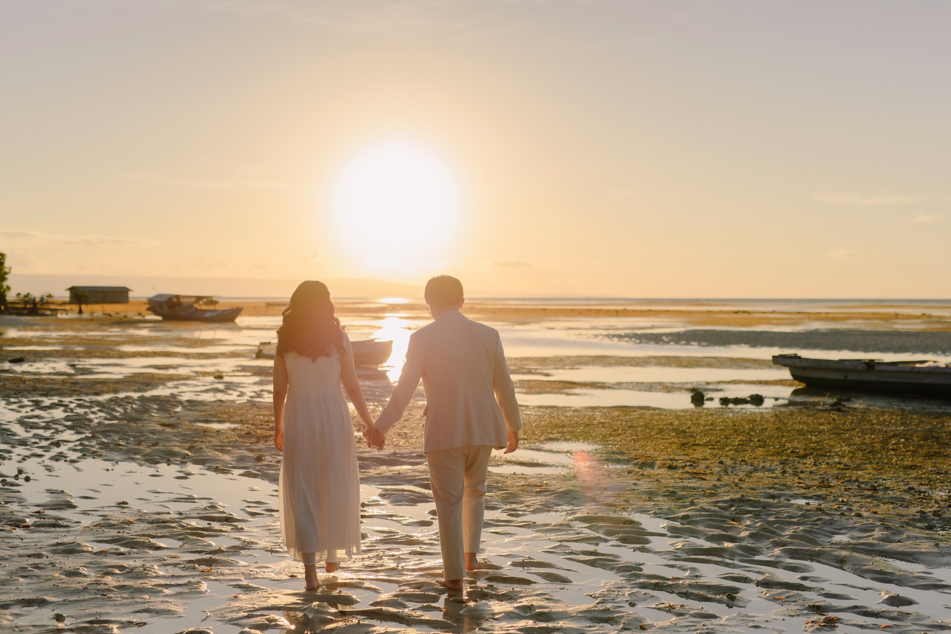 Rey and Feli holding hands as they walk toward the sunset on the beach