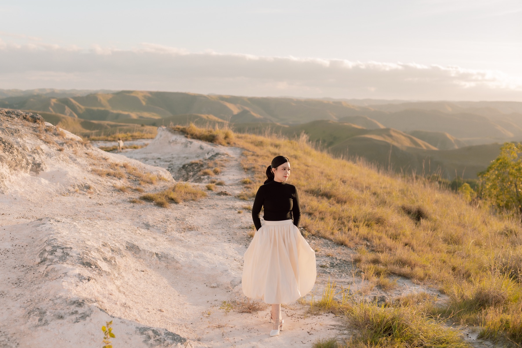 Feli standing on a pale rocky hill with golden valleys behind her