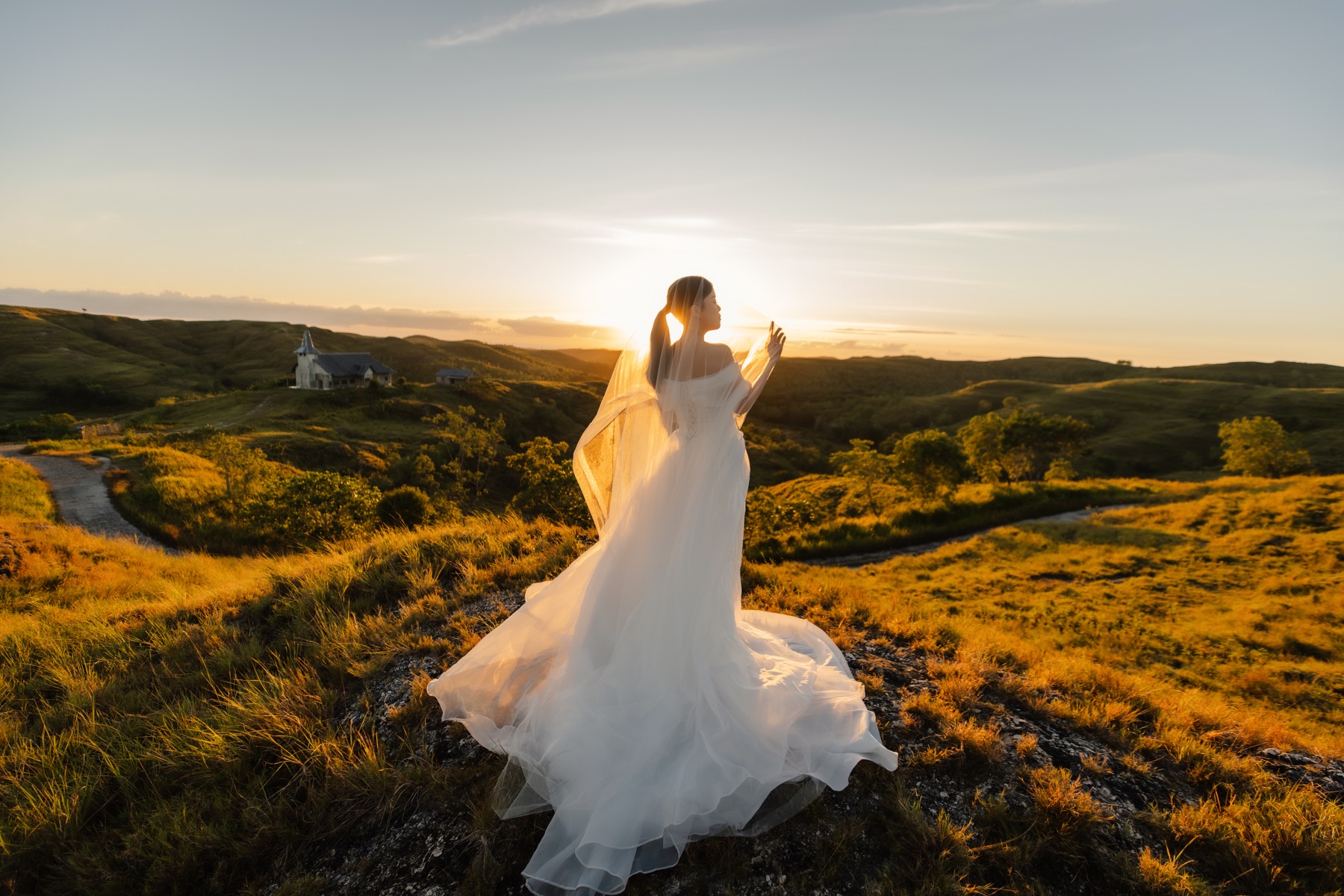 Feli facing a golden hillside as her wedding dress catches the evening light