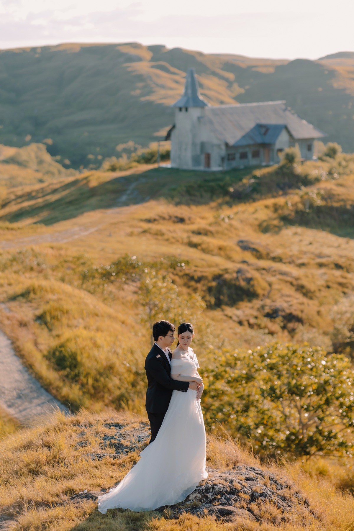 Rey and Feli embracing on a golden hill below a small white chapel